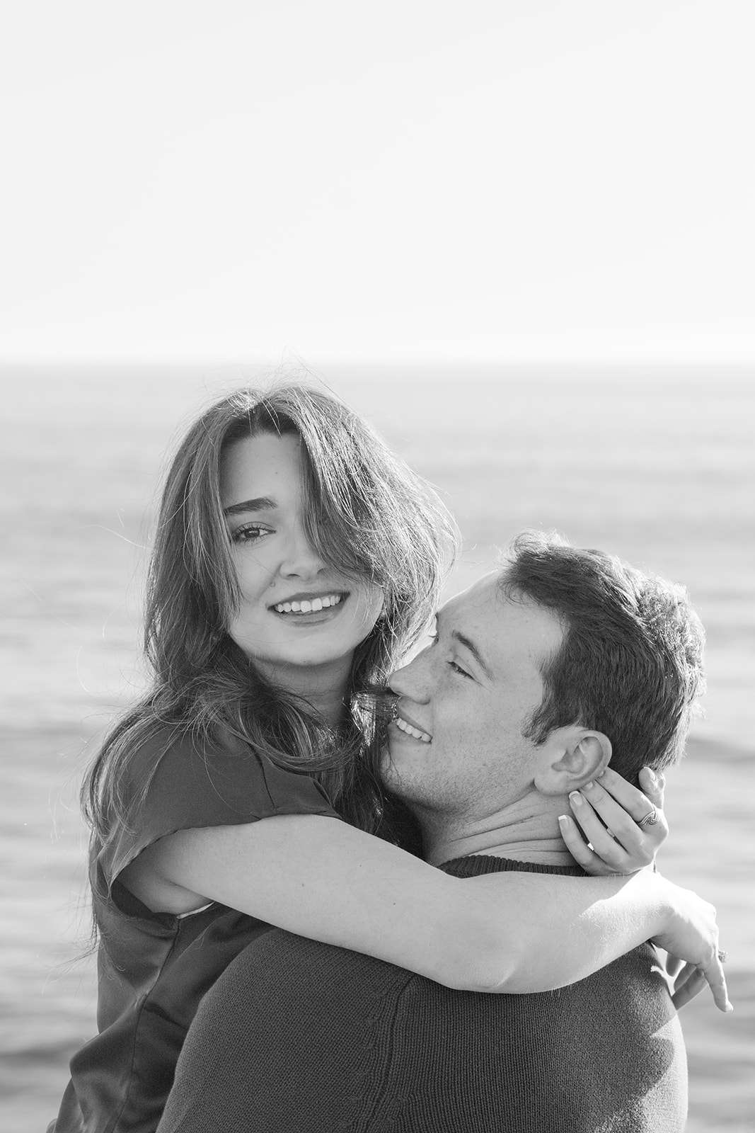 Black and white photo of a couple on a Santa Cruz cliffside overlooking the ocean at sunset.