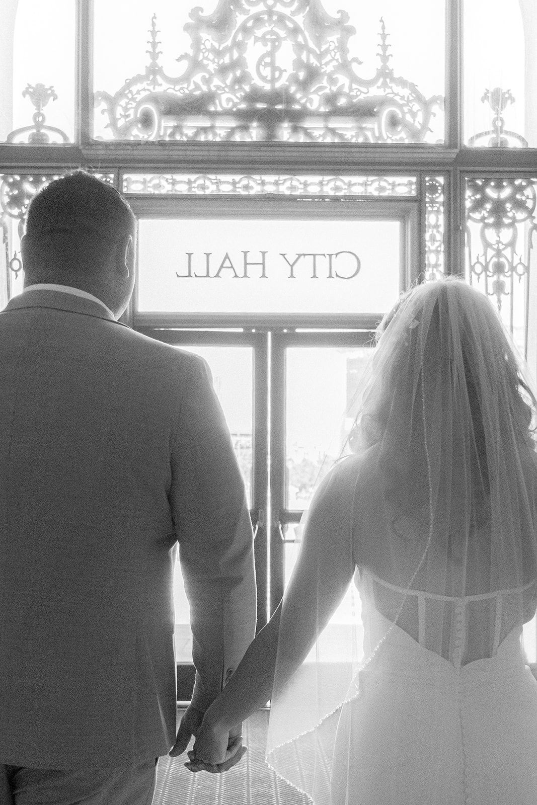 Bride and groom exiting beneath a sign at San Francisco City Hall after their wedding.