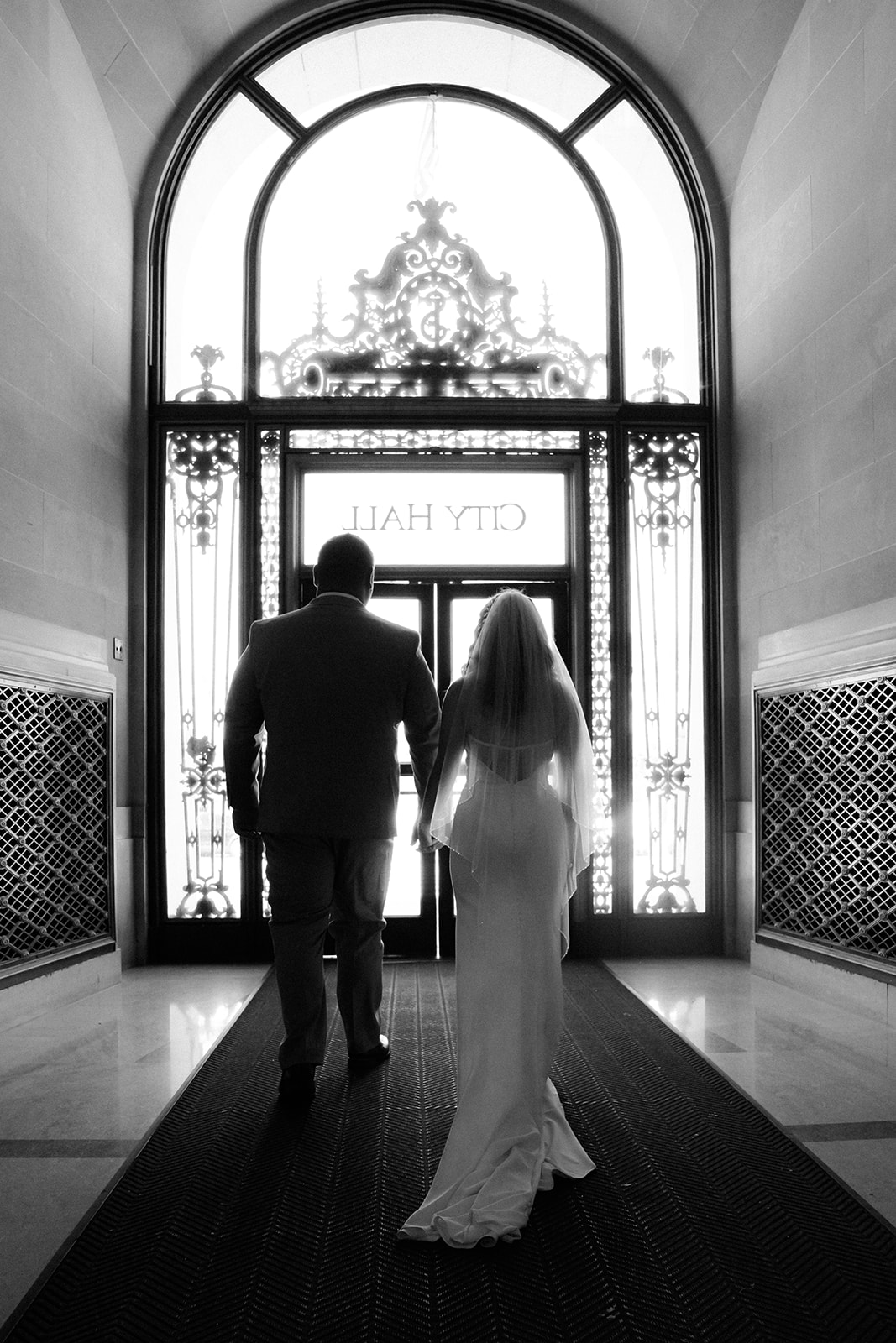 Bride and groom exiting San Francisco City Hall beneath a sign after their wedding.