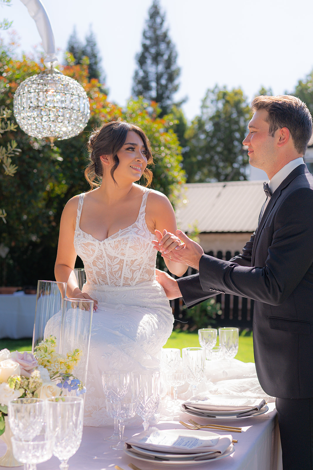 Bride and groom posing together on a decorated garden wedding reception table at Rainbow Oaks Ranch in Sanger, California.