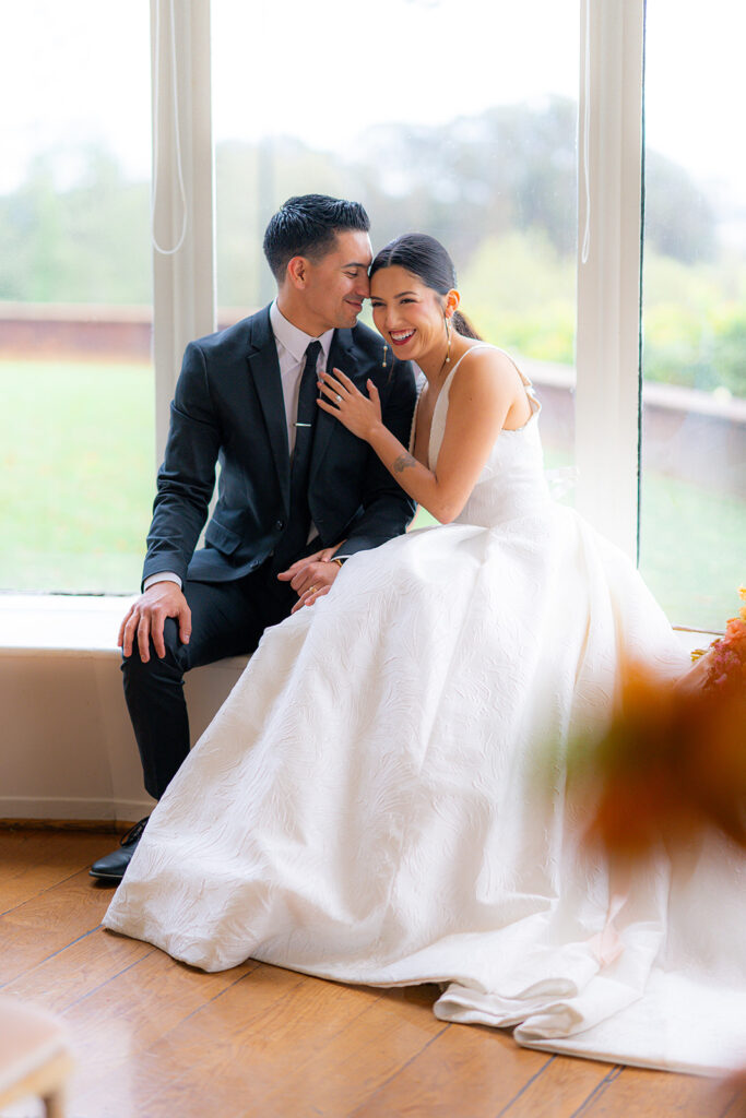 Bride and groom sitting together in a window, laughing and smiling at Hollins House in Santa Cruz, California.
