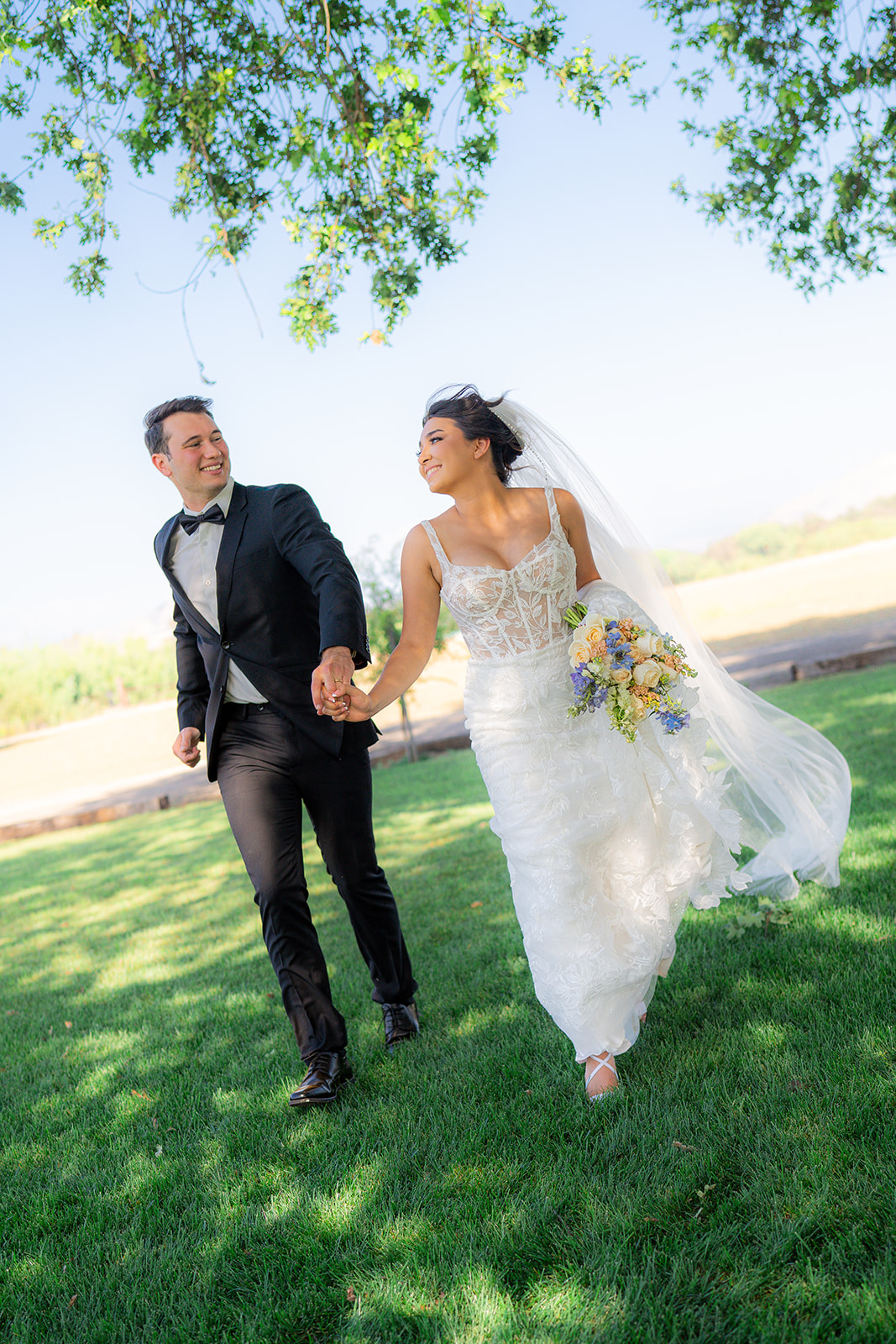 Bride and groom running together beneath an oak tree at Rainbow Oaks Ranch in Sanger, California.
