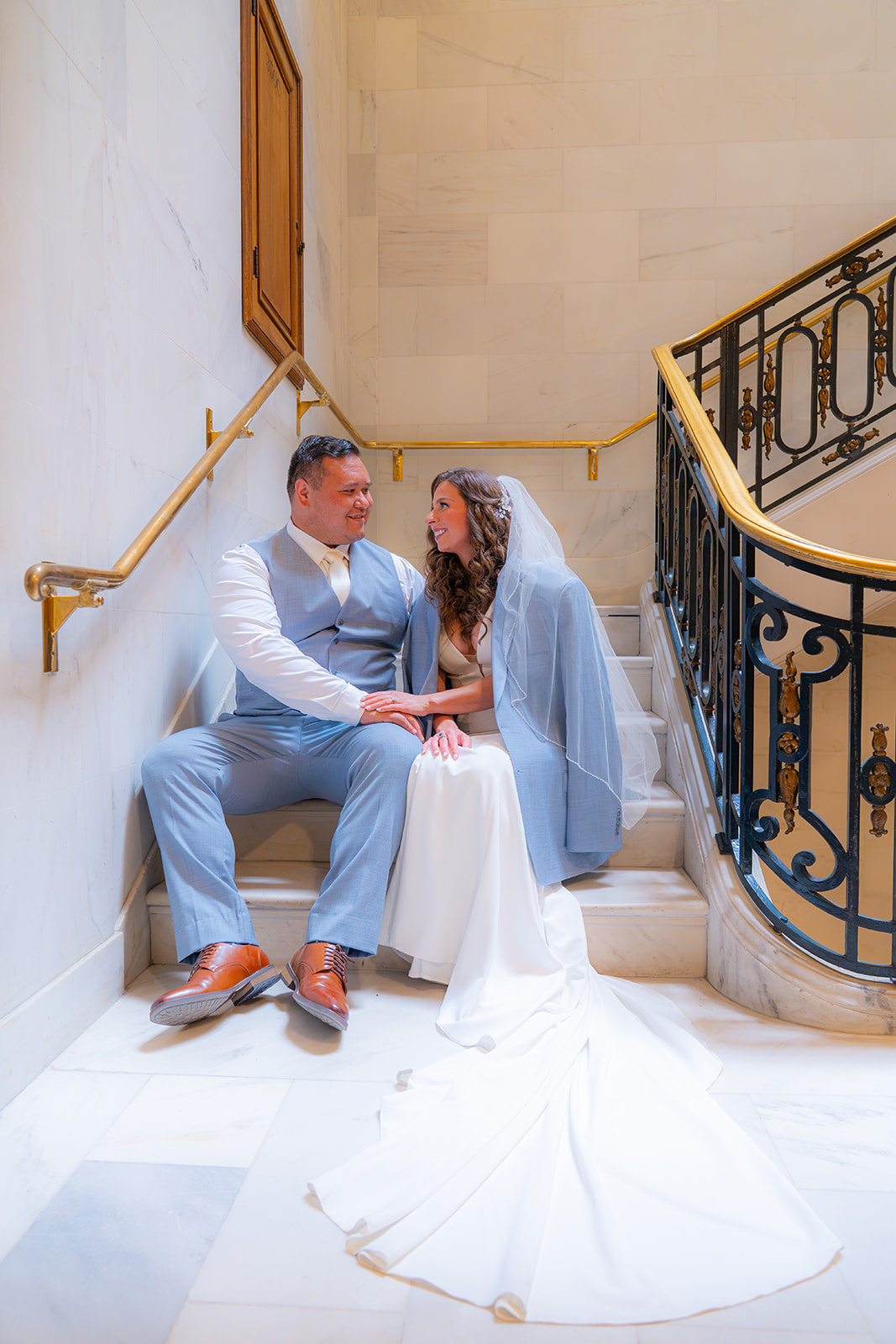Bride and groom sitting together on a staircase at San Francisco City Hall during their wedding.