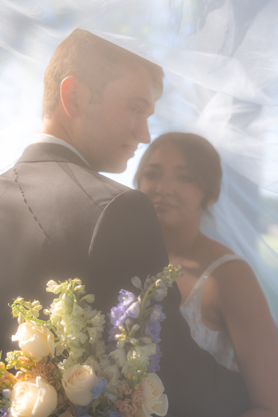 Bride and groom smiling together beneath the bride’s wedding veil during a garden wedding at Rainbow Oaks Ranch in Sanger, California.