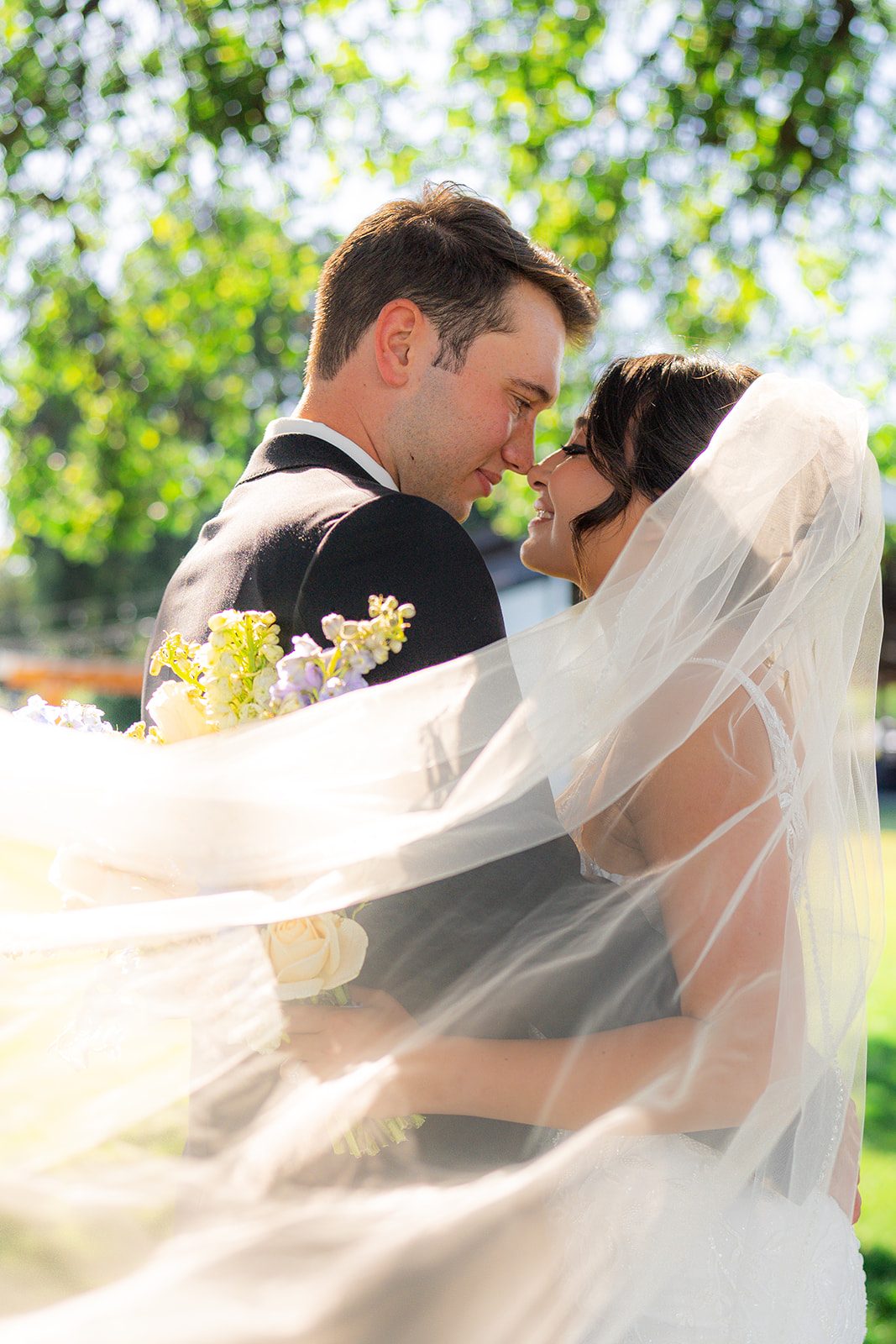 Bride and groom posing together as the bride’s wedding veil sweeps through the air at Rainbow Oaks Ranch in Sanger, California.