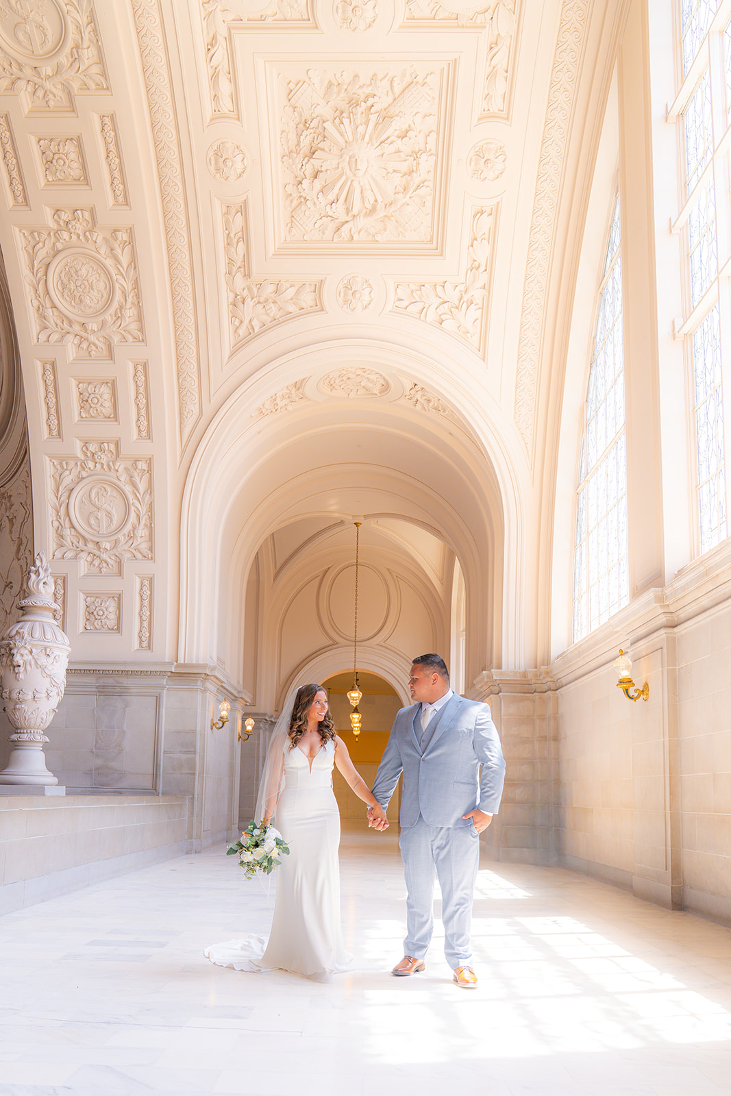 Bride and groom walking together through a hallway at San Francisco City Hall during their wedding.