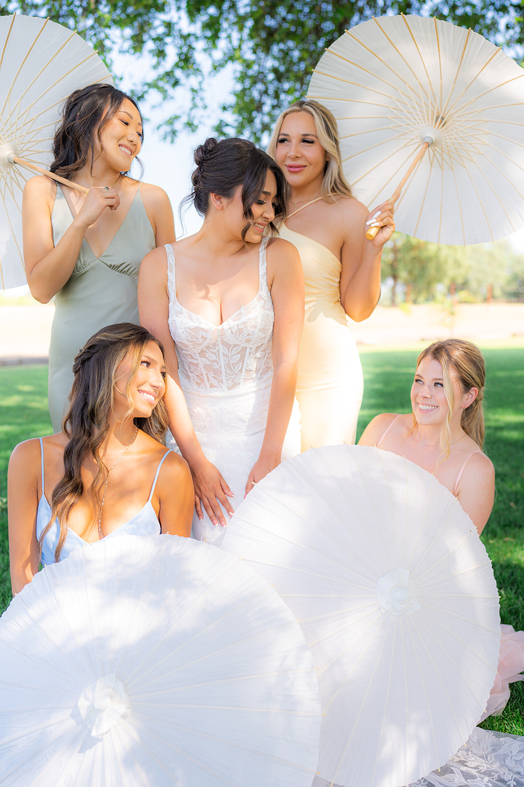 Bride and bridesmaids in pastel dresses posing with parasol umbrellas beneath a tree at Rainbow Oaks Ranch in Sanger, California.