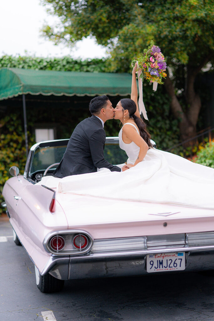 Bride and groom sharing a celebratory kiss during their classic car wedding exit at Hollins House in Santa Cruz, California.