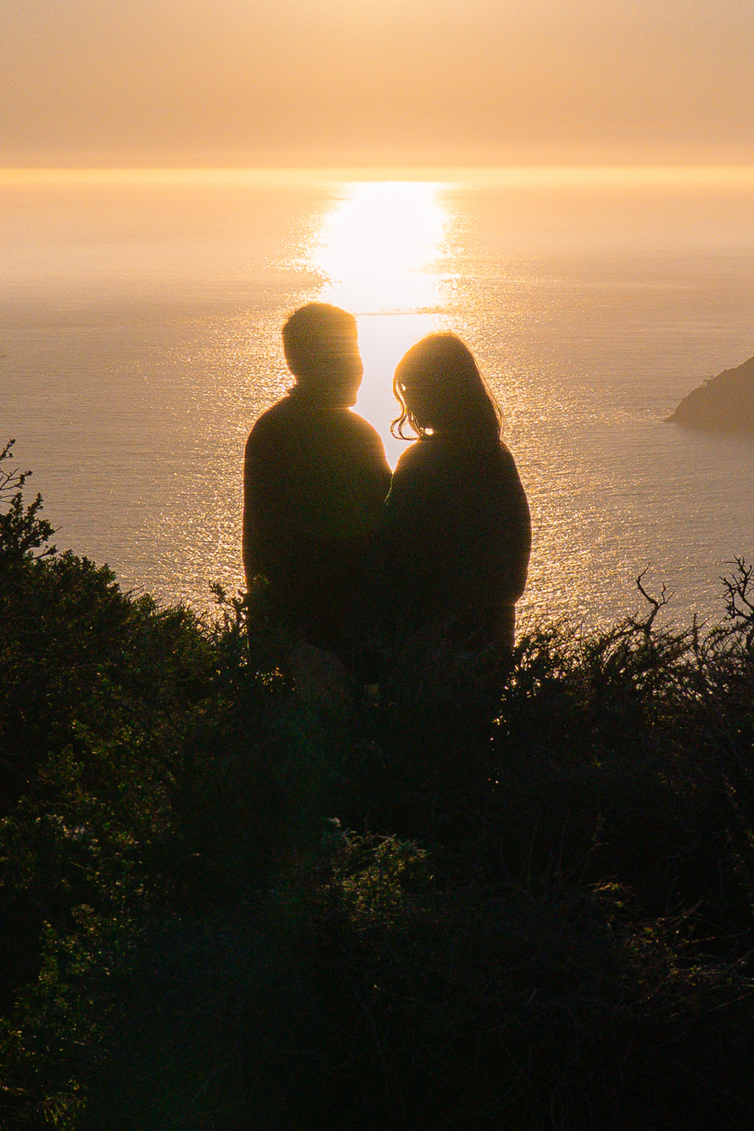 Couple standing in golden sunlight on a scenic cliffside overlooking the ocean near San Francisco.