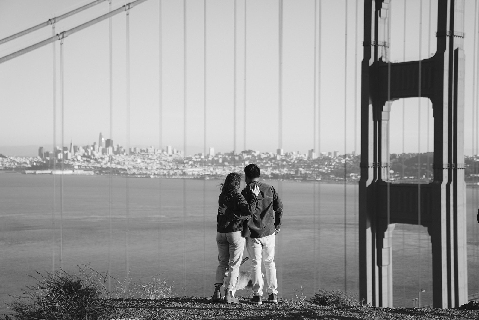 Couple embracing at Battery Spencer with scenic views near the Golden Gate Bridge.