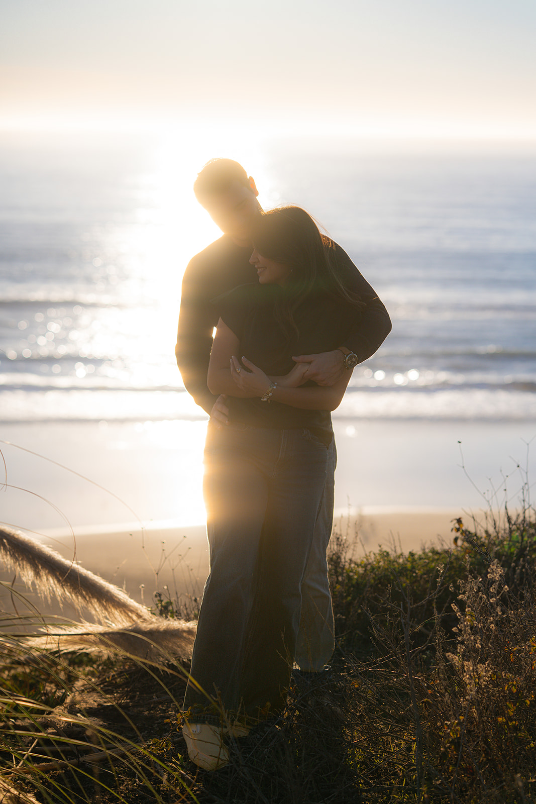Couple embracing on a Santa Cruz cliffside with the ocean sparkling in the sunset light.