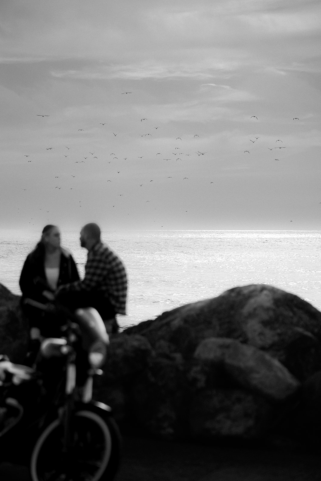 Black and white photo of a couple embracing on coastal rocks during a motorcycle couples session at Pacifica State Beach