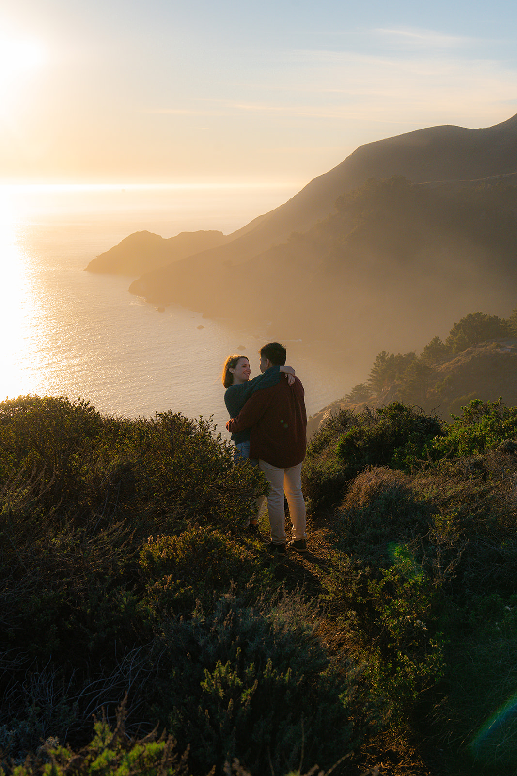 Couple laughing together on a scenic cliffside overlooking the ocean at sunset near San Francisco.