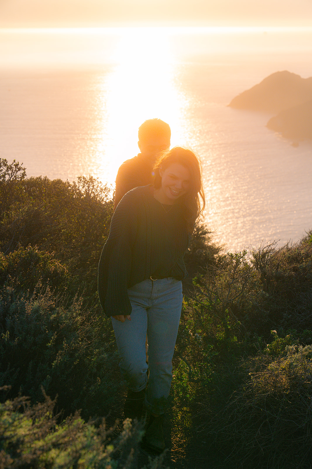 Couple with their dog on a scenic cliffside during golden hour near San Francisco.