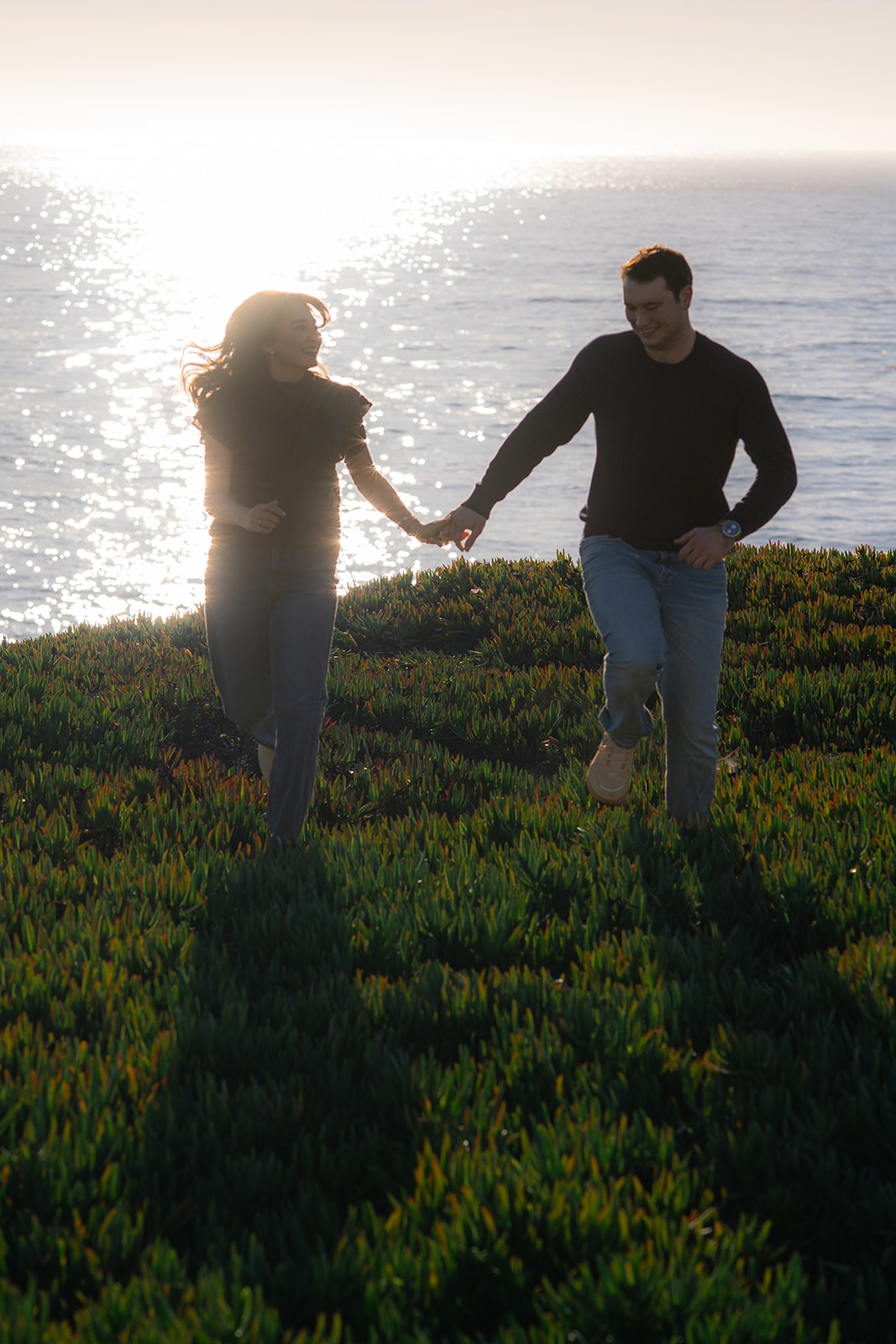 Couple running together along a scenic cliffside in Santa Cruz, California.