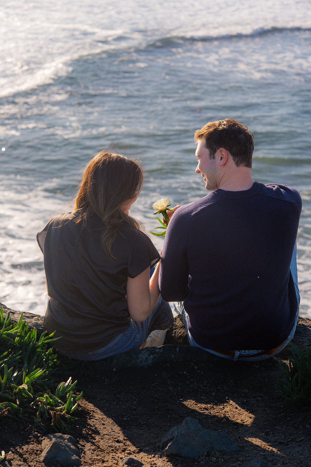 Couple sitting with a flower on a scenic Santa Cruz cliffside overlooking the ocean.
