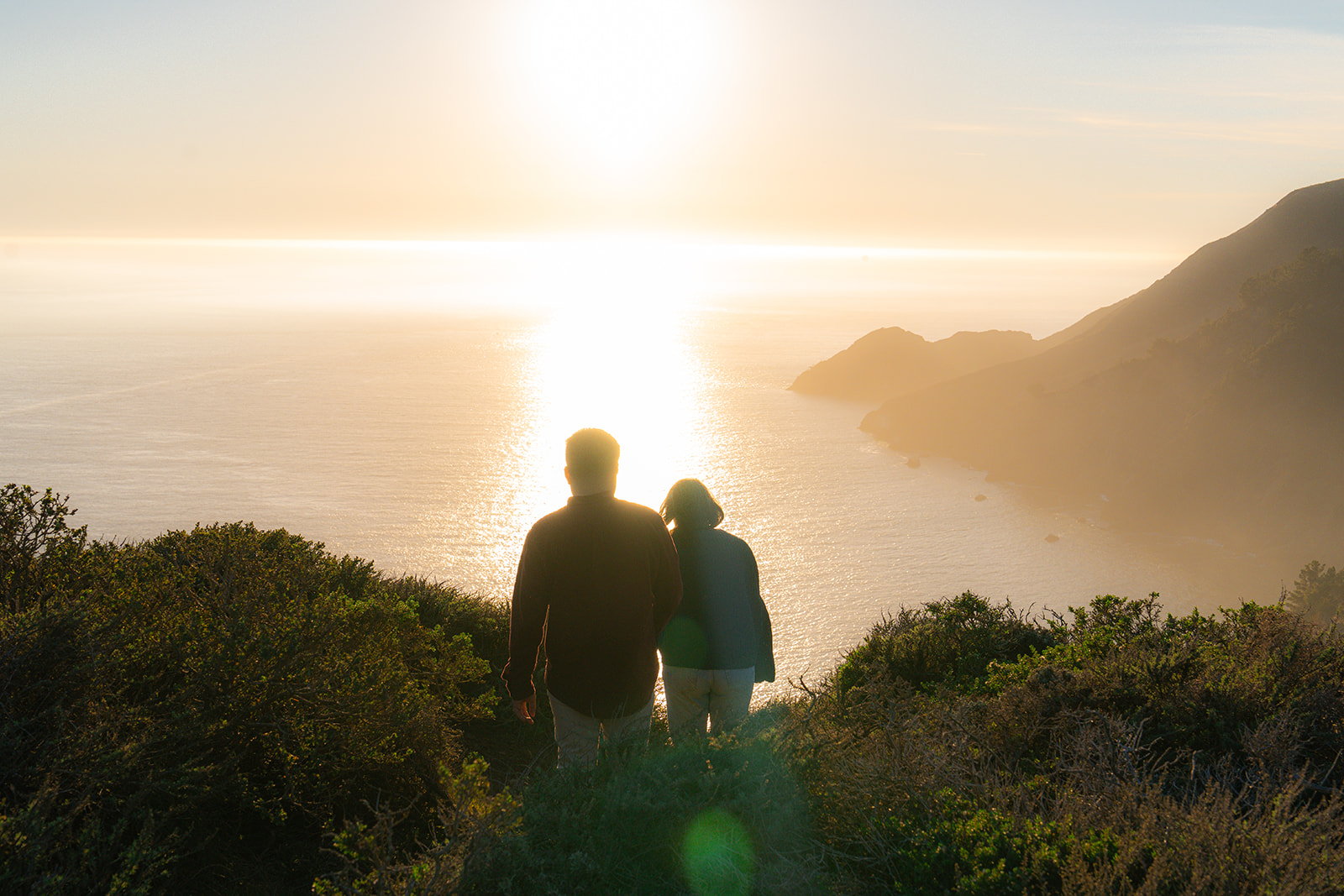 Couple walking into the sunset on a scenic cliffside overlooking the ocean in San Francisco.