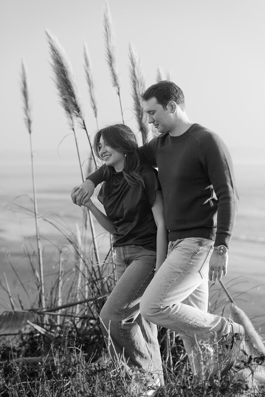 Black and white photo of a couple walking along a Santa Cruz beach beside coastal grass.