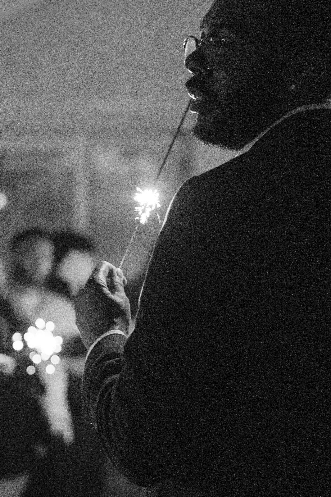 Candid photograph of a groom holding a lit sparkler in front of wedding guests at Fairview Metropolitan in Oakland, California.