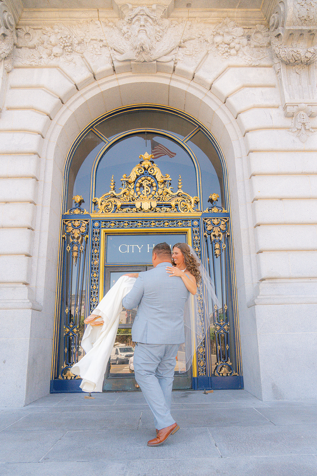 Groom carrying the bride in front of San Francisco City Hall during their wedding.