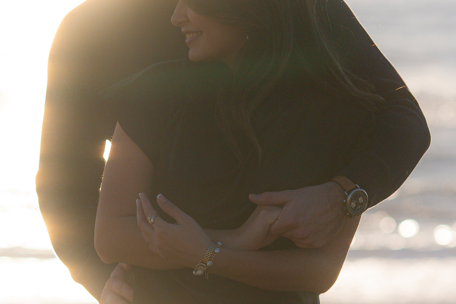 Couple embracing on a Santa Cruz cliffside with the ocean sparkling in the sunset behind them.