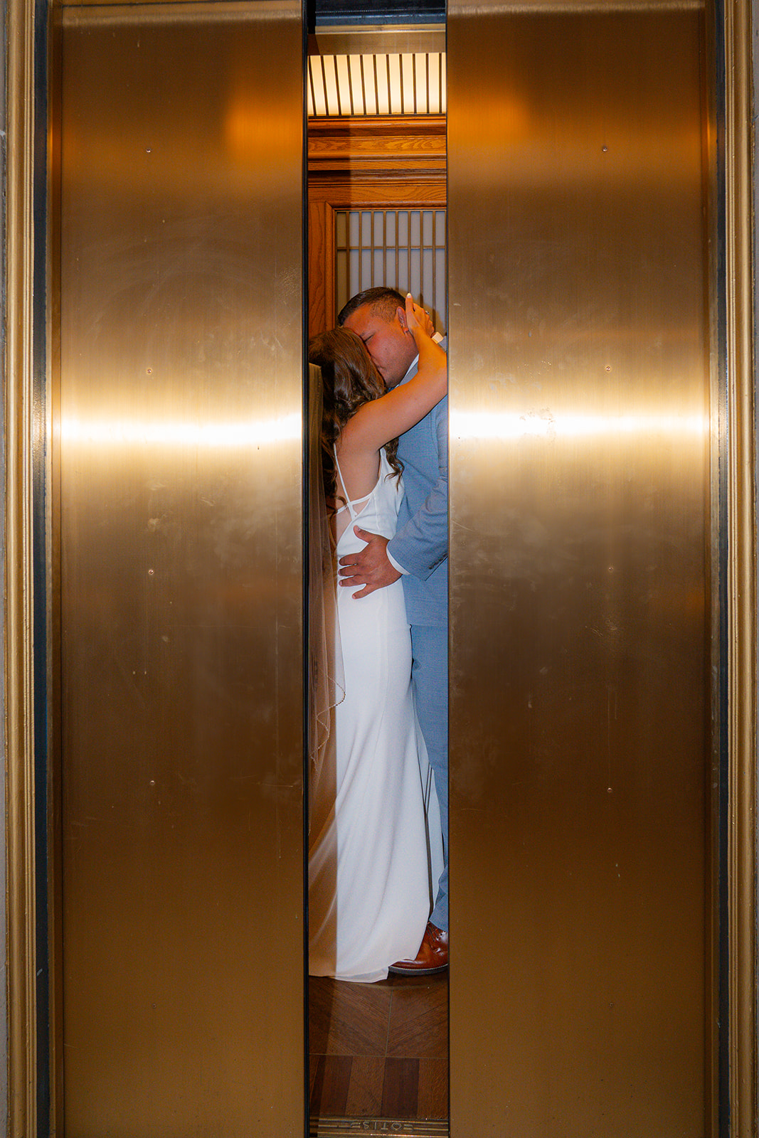 Bride and groom sharing a kiss in front of gold elevator doors at San Francisco City Hall.