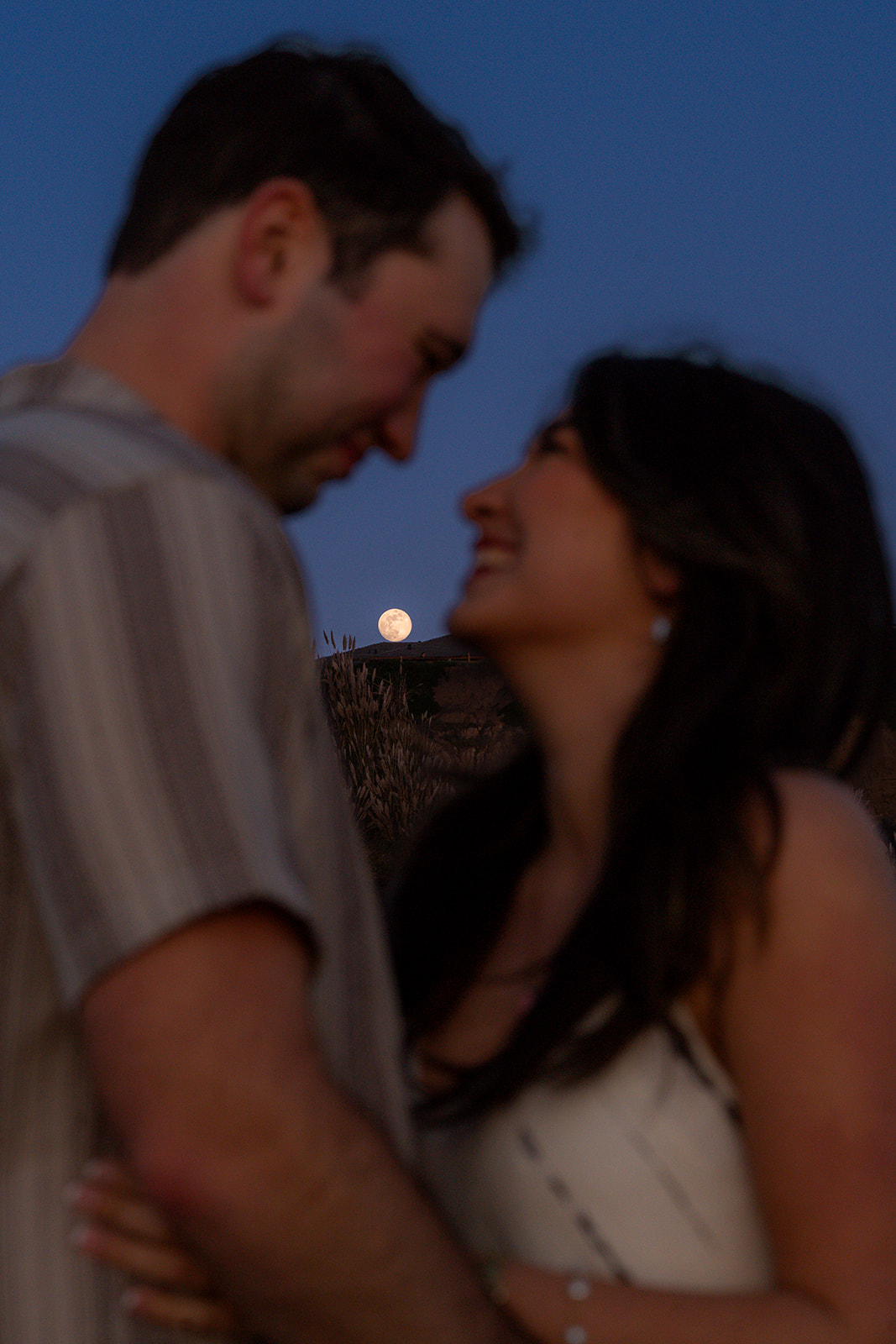 Moonlit couple on a Santa Cruz beach with the moon glowing behind them.