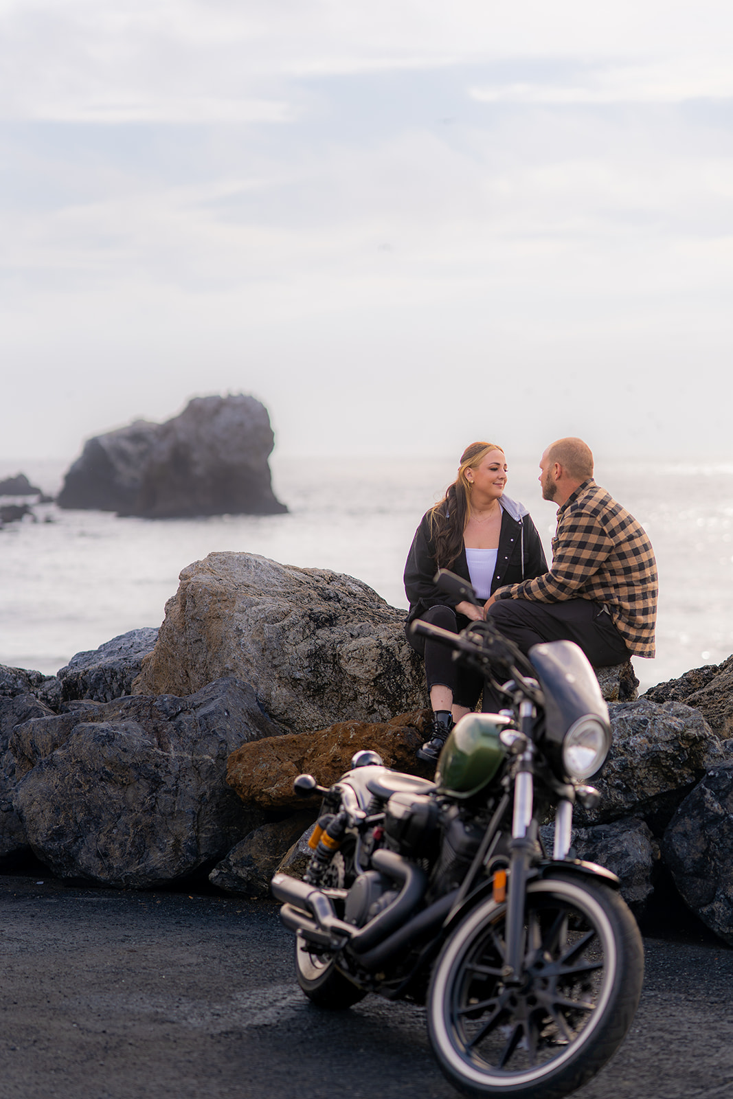 Couple sitting together on coastal rocks during a motorcycle couples photoshoot at Pacifica State Beach