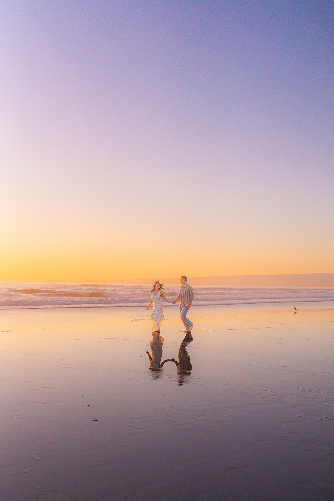 Couple running barefoot along the ocean on a beach in Santa Cruz.