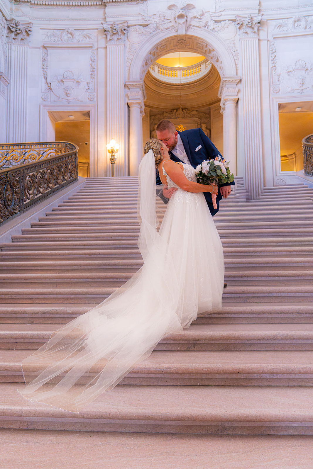 Bride and groom kissing on the grand staircase inside San Francisco City Hall on their wedding day