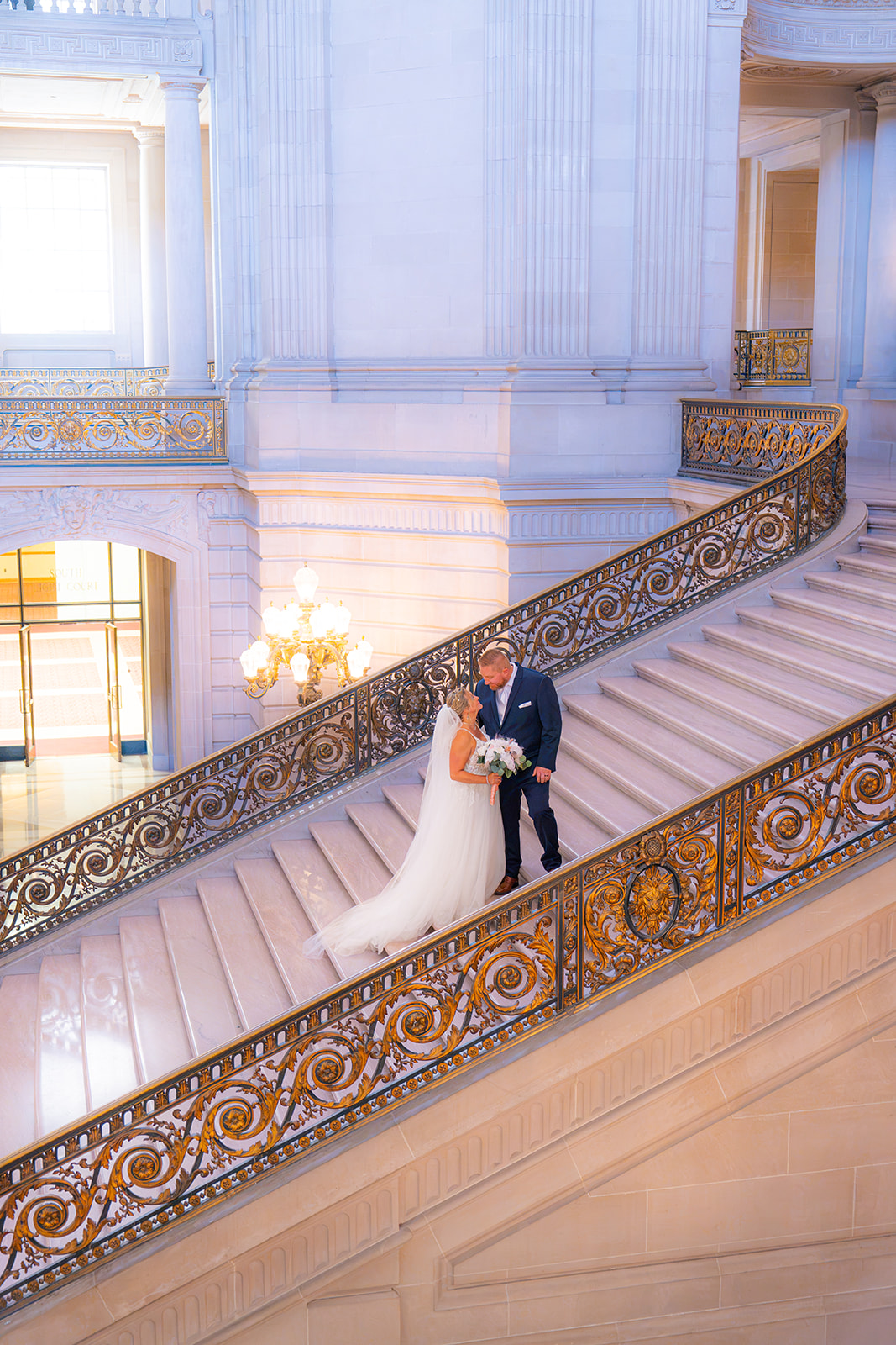 Bride and groom together on the grand staircase inside San Francisco City Hall on their wedding day
