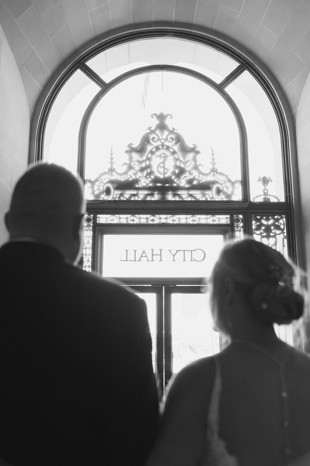 Newlywed couple exiting San Francisco City Hall with the City Hall sign visible above them