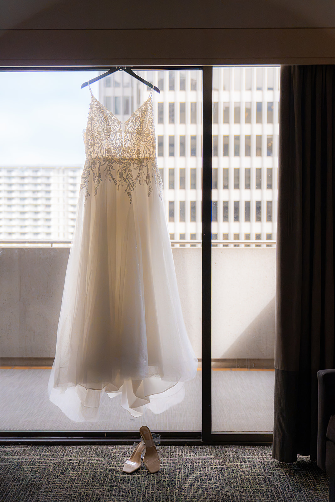 Wedding dress hanging in a San Francisco hotel sliding glass door with city buildings visible outside