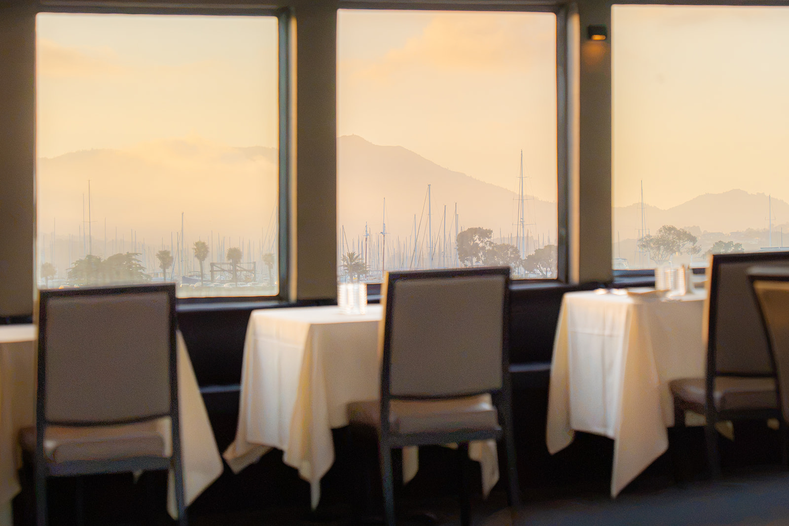Cream-colored chairs inside a San Francisco wedding dinner cruise with mountains and palm trees visible through the windows