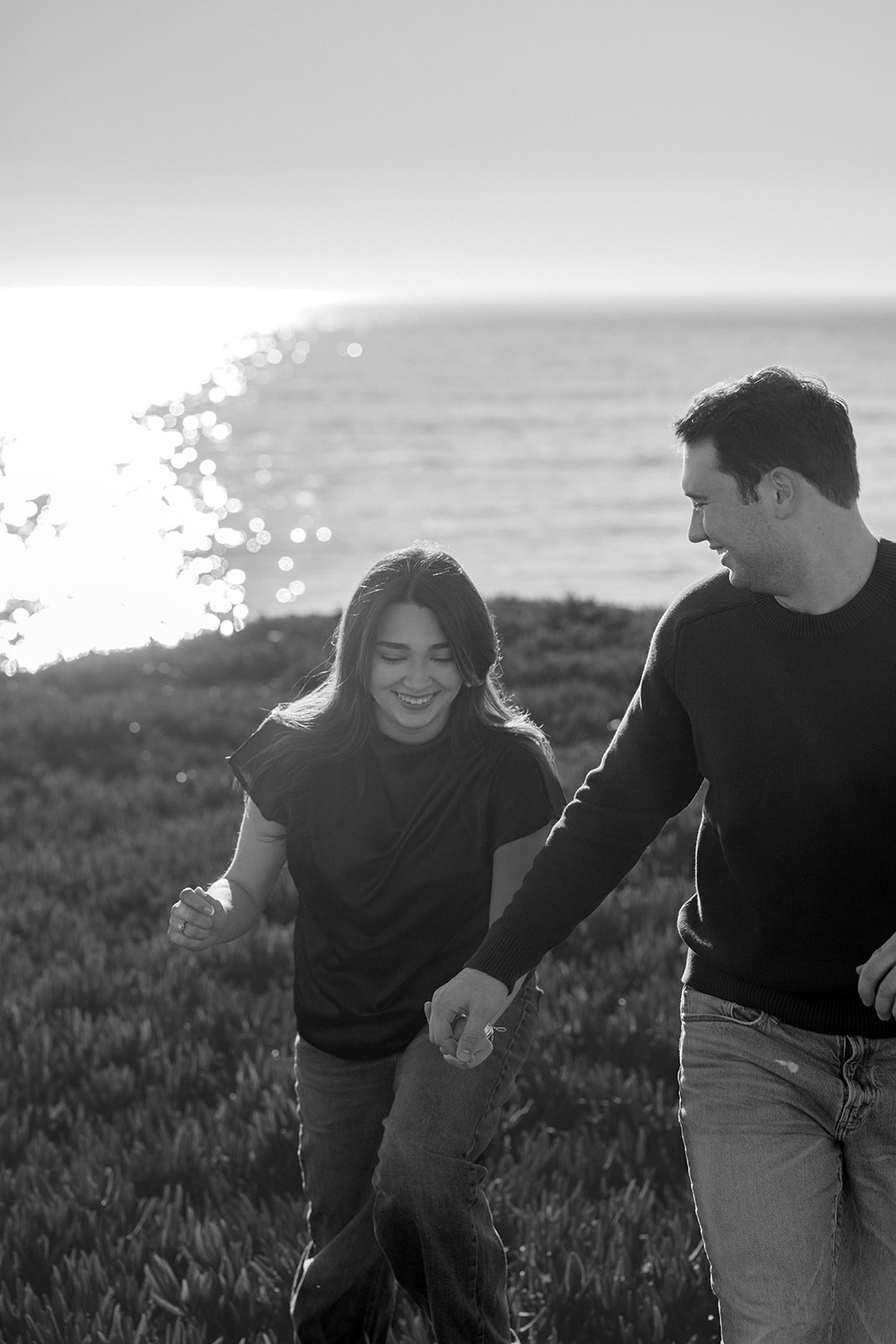 Couple running together on a scenic cliffside overlooking the coast in Santa Cruz.