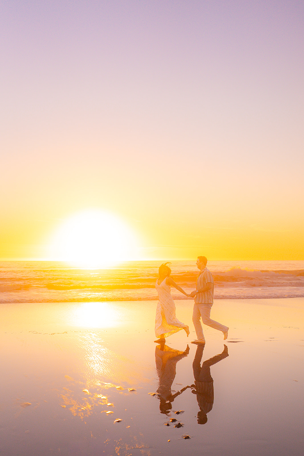 Couple running barefoot across the sand at sunset on a beach in Santa Cruz.