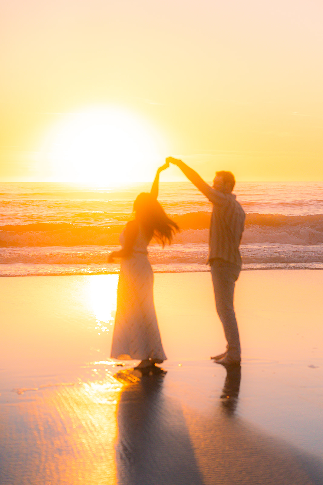 Couple twirling barefoot on the sand at sunset on a beach in Santa Cruz.