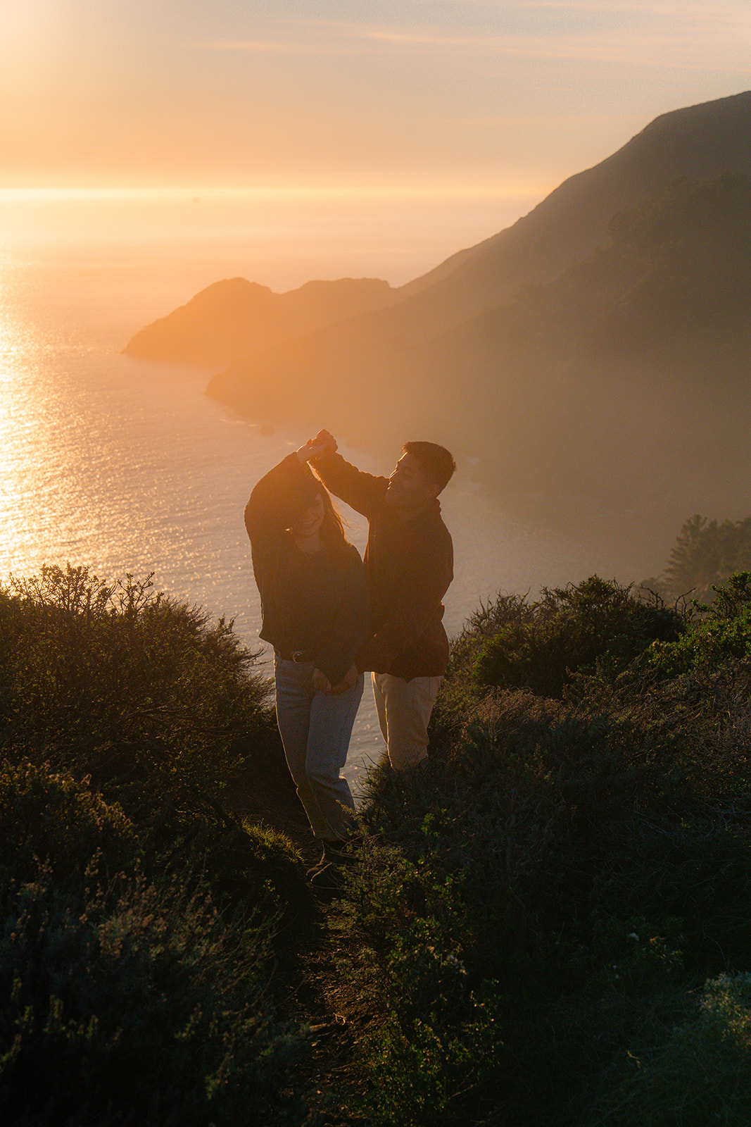 Couple dancing in golden sunlight on a cliffside overlooking the ocean at sunset in San Francisco.