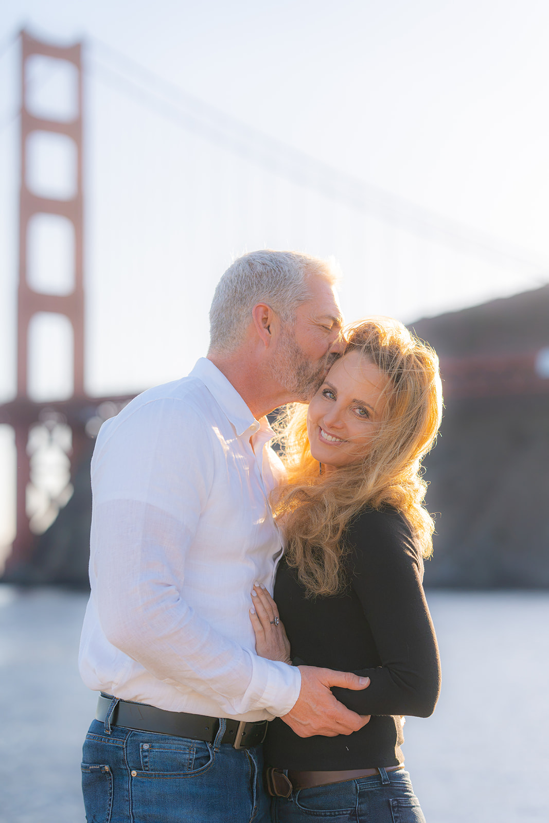 Couple posing for sunset photos by the San Francisco Bay with the Golden Gate Bridge in the background