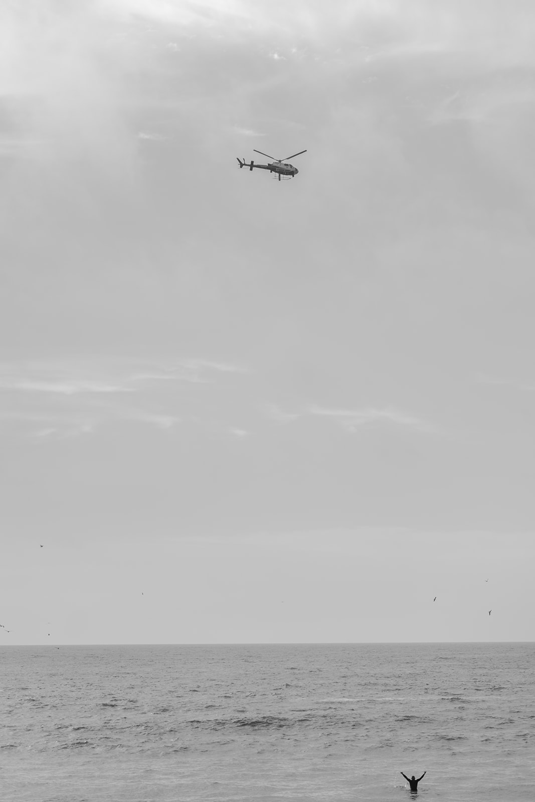 Surfer in the ocean and helicopter overhead during a motorcycle engagement session at Pacifica State Beach in California