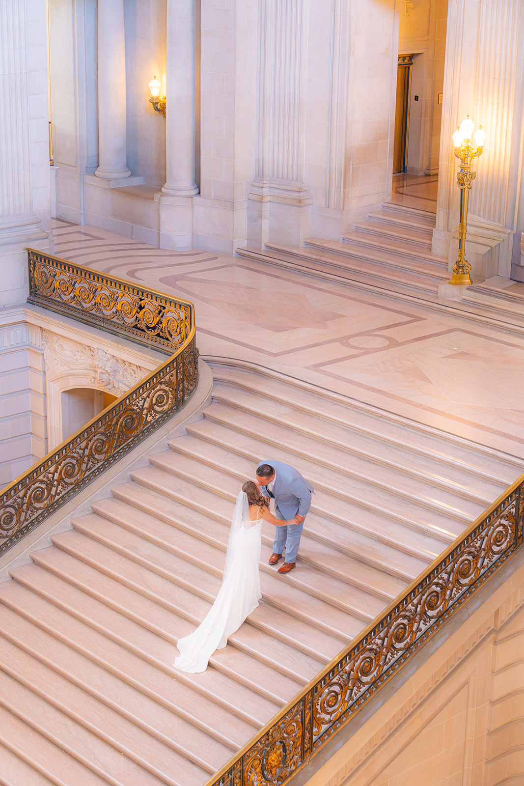 Bride and groom kissing on the grand staircase at San Francisco City Hall during their wedding.