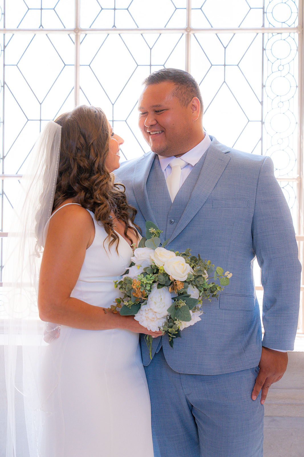Bride and groom standing together in front of a window at San Francisco City Hall during their wedding.