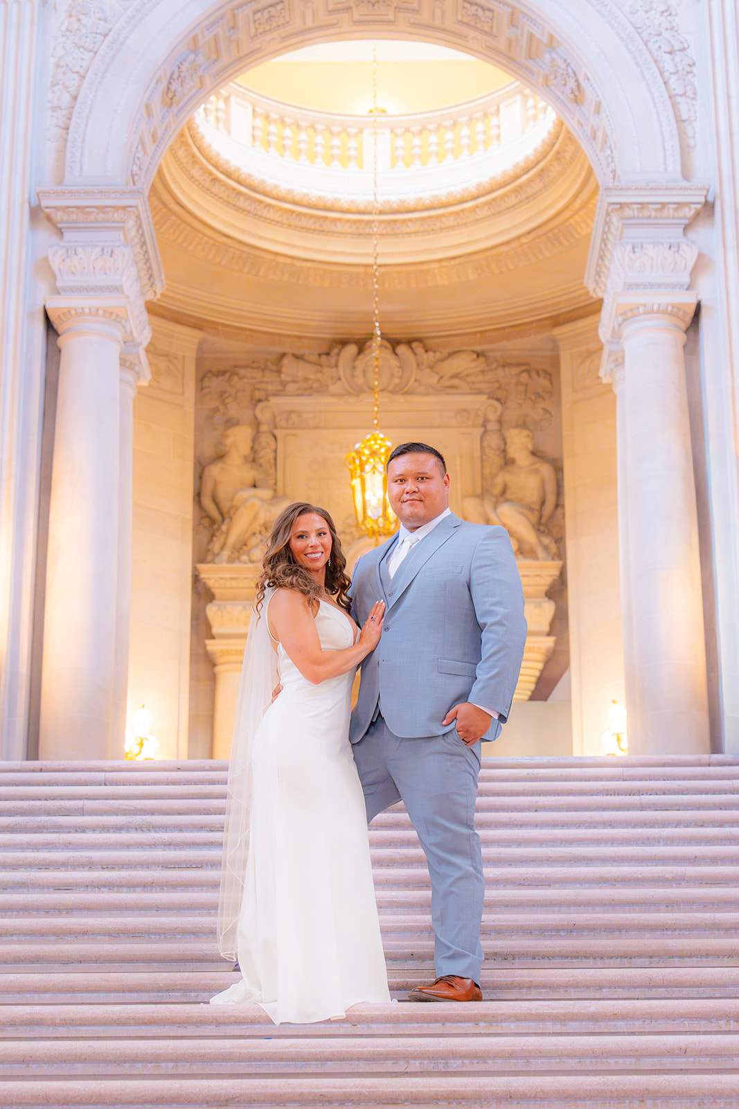 Bride and groom standing together on the stairs at San Francisco City Hall during their wedding.